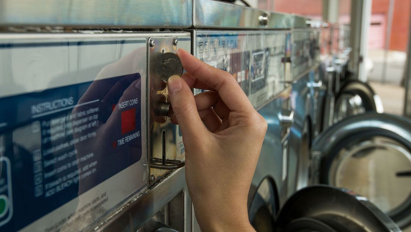 woman inserting coin into a washing machine in a laundrette